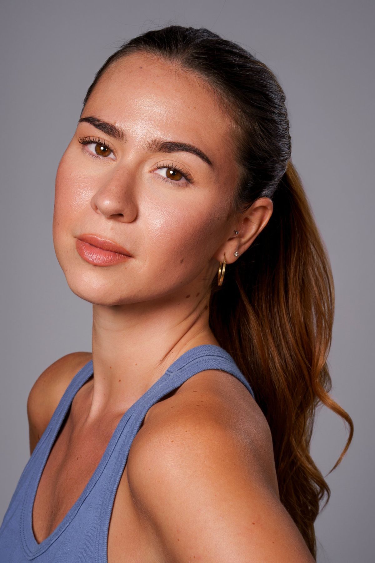 Headshot in blue tank top, hair pulled back, looking over shoulder