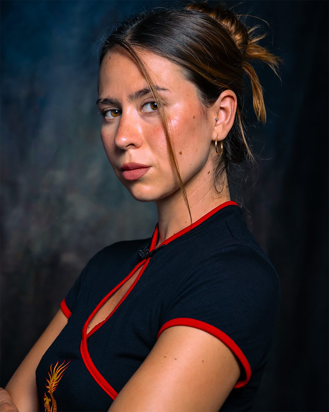 Portrait against a dark painted backdrop, hair half up, looking over shoulder
